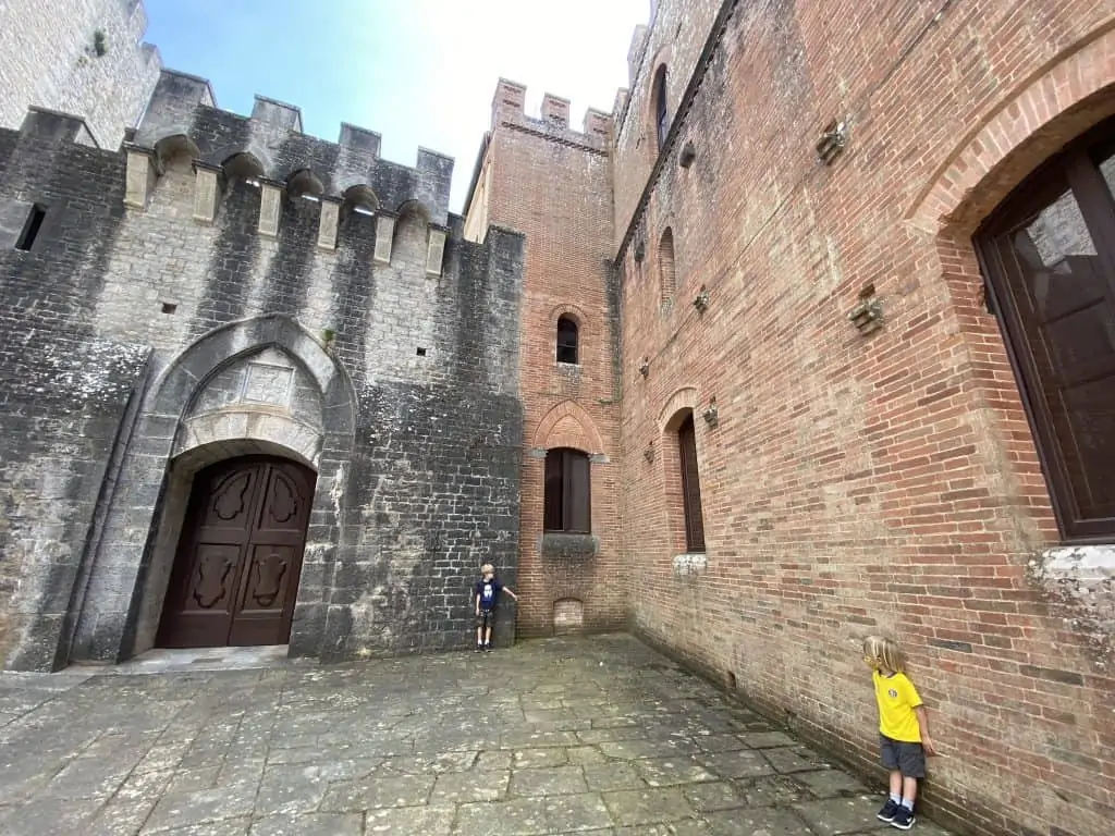 Boys stand next to walls at castle. The walls are different colors - grey and orange.