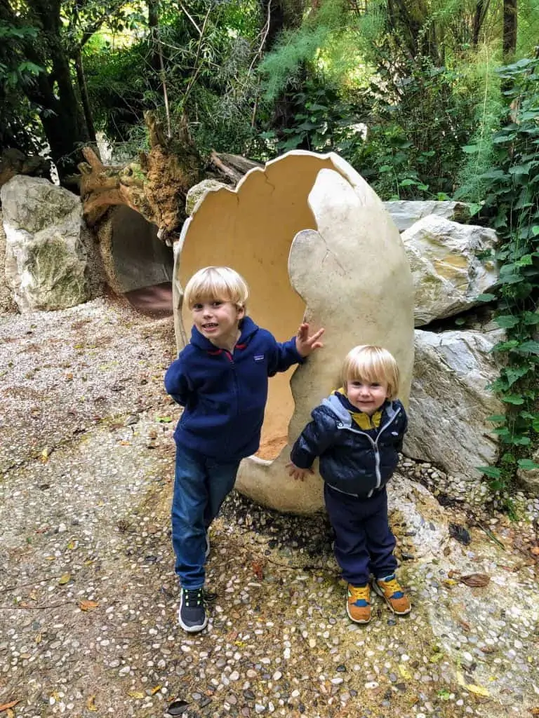two blond little boys posing in front of a large replica of a dinosaur egg at the zoo di pistoia in italy