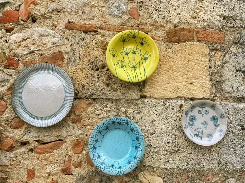 Four colorful ceramic plates hang on a stone wall outside a shop in Monteriggioni, Italy.