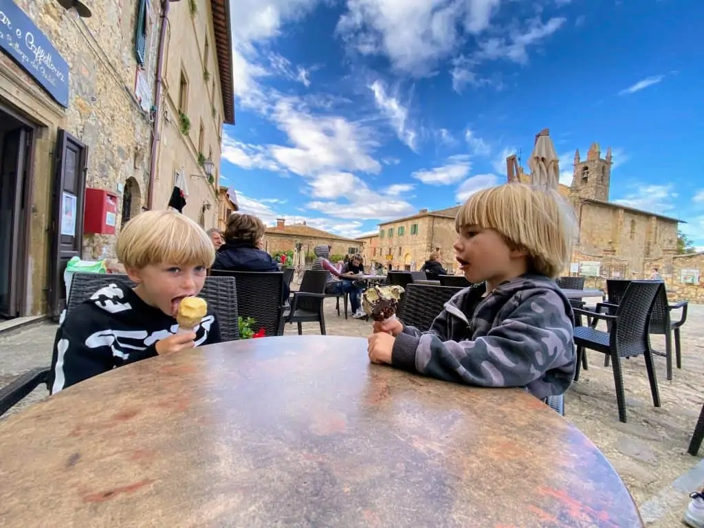 Two boys eating gelato at a table in Piazza Roma in Monteriggioni, Italy.