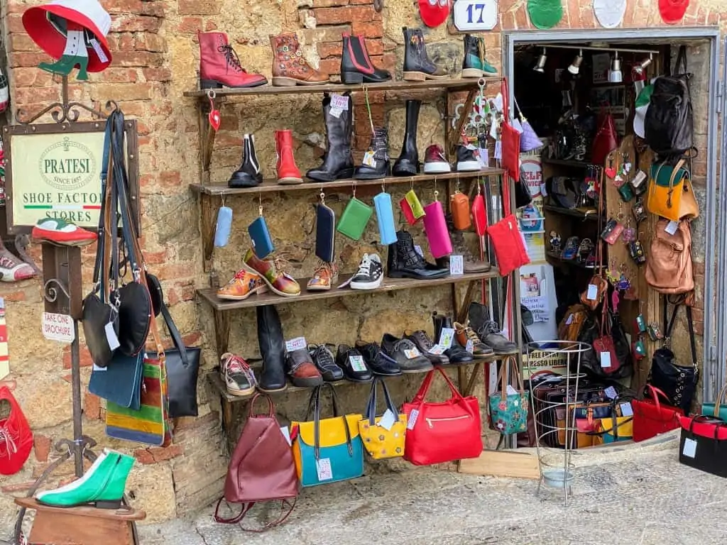 Entrance to Pratesi leather shop in Monteriggioni Italy.  Colorful shoes, wallets, and handbags are displayed on a rack outside and in the doorway.