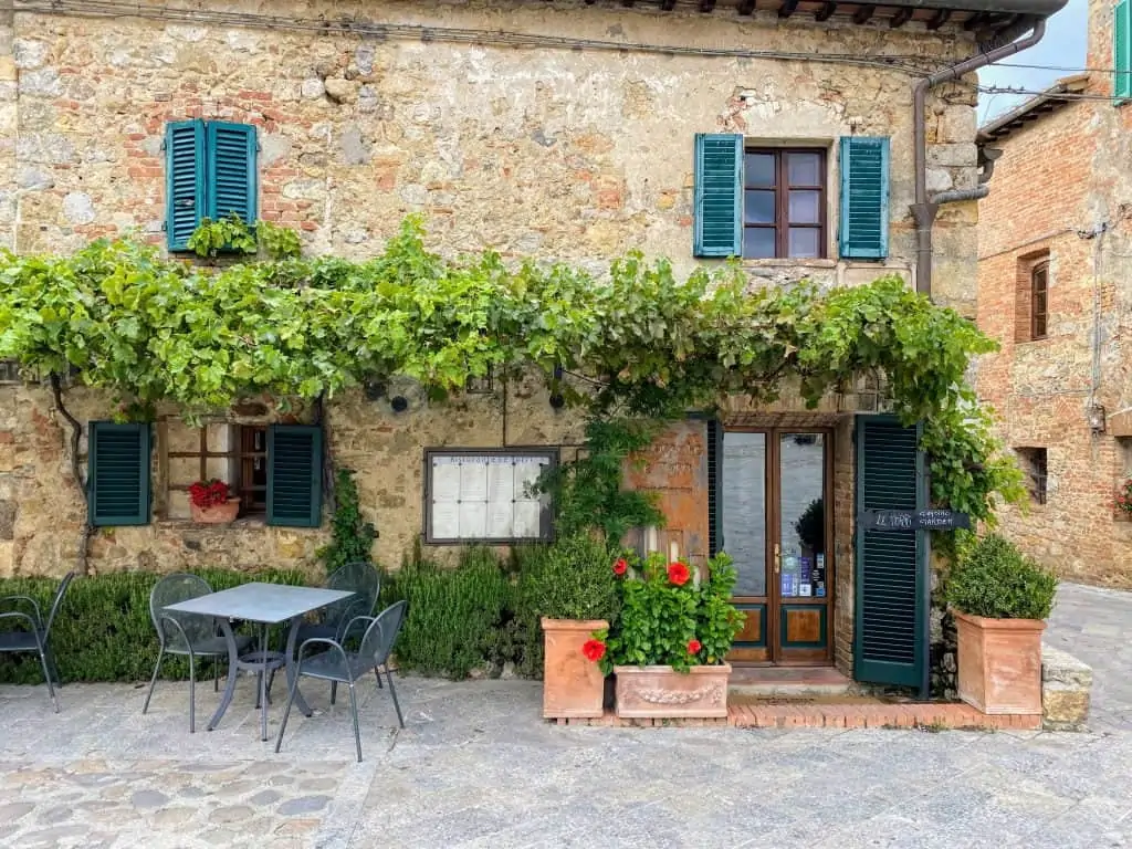 Ristorante Le Torri entrance with talbes and chairs and vines on the stone walls in Monteriggioni, Italy.