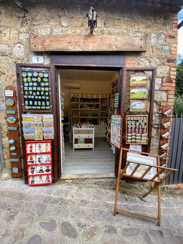 A souvenir shop in Monteriggioni, Italy with displays of postcards, magnets, paintings, and cards.