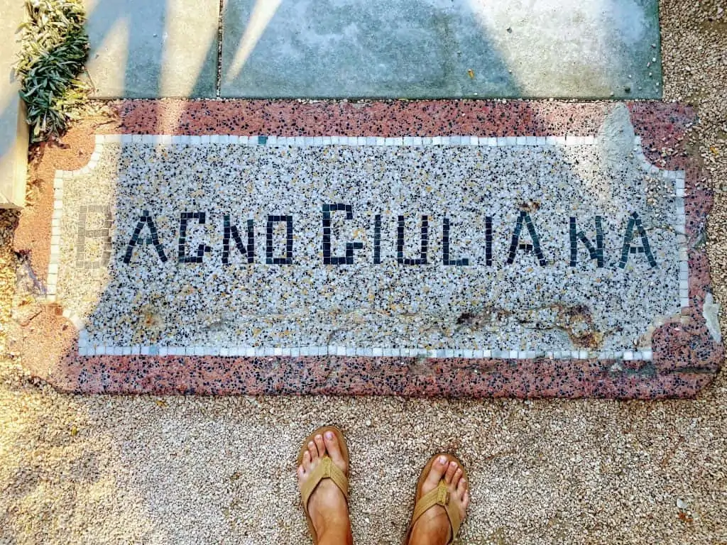 close up of mosaic 'bagno giuliana' sign with feet in flip flops below it