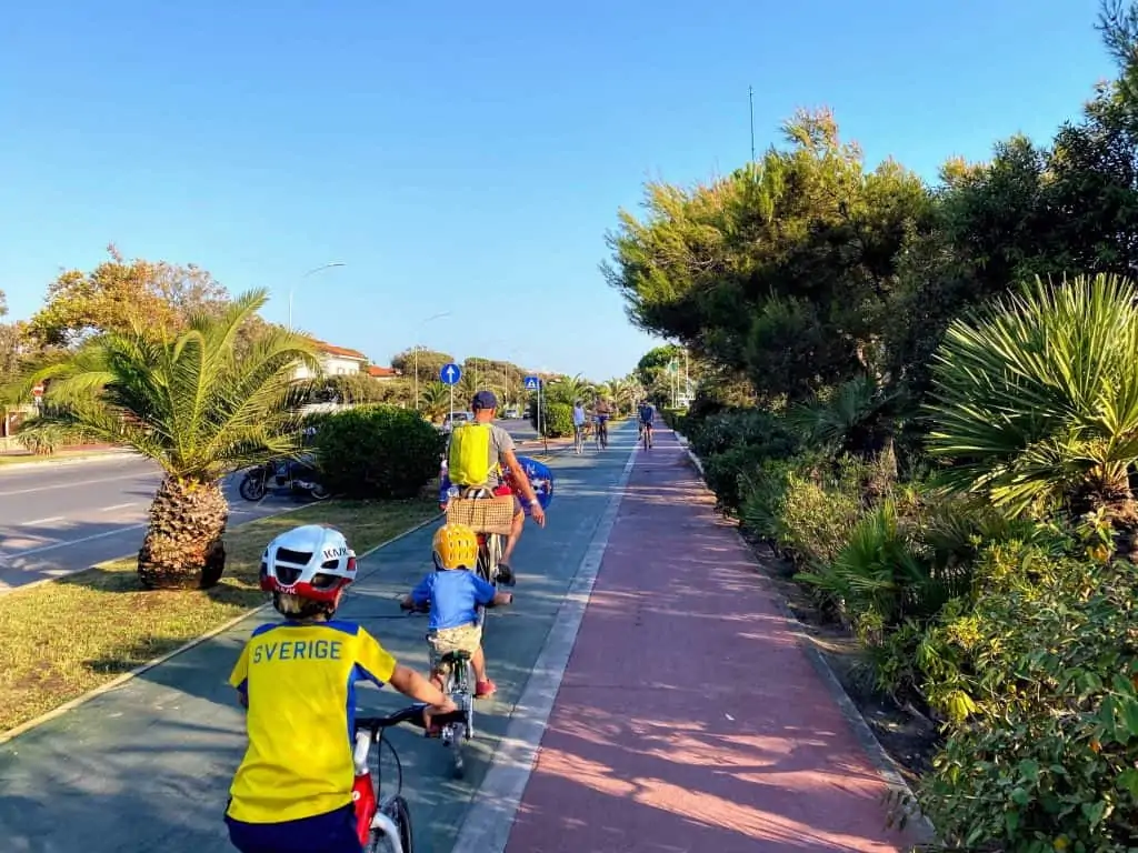 man and two small boys facing away from the camera, riding their bicycles down the bike path in forte dei marmi, italy