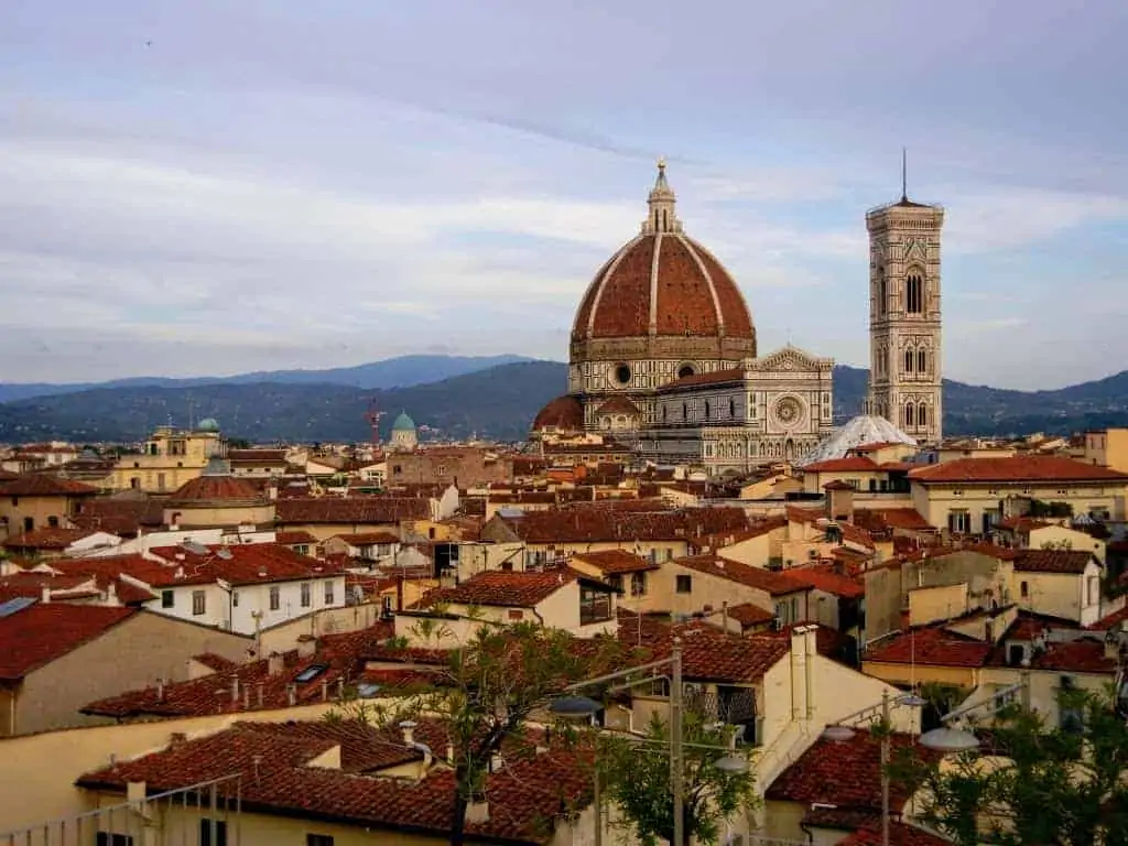 View of the Duomo and belltower of Florence, Italy as the sun goes down.  Grey sky, other red-roofed buildings in the foreground.