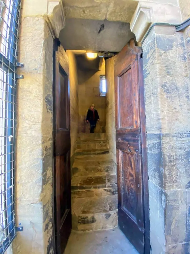 Boy facing the camera at the top of a flight of stairs in Giotto's bell tower in Florence, Italy.  The stairs are stone and narrow.  The bottom of the stairs is framed by open wooden doors.