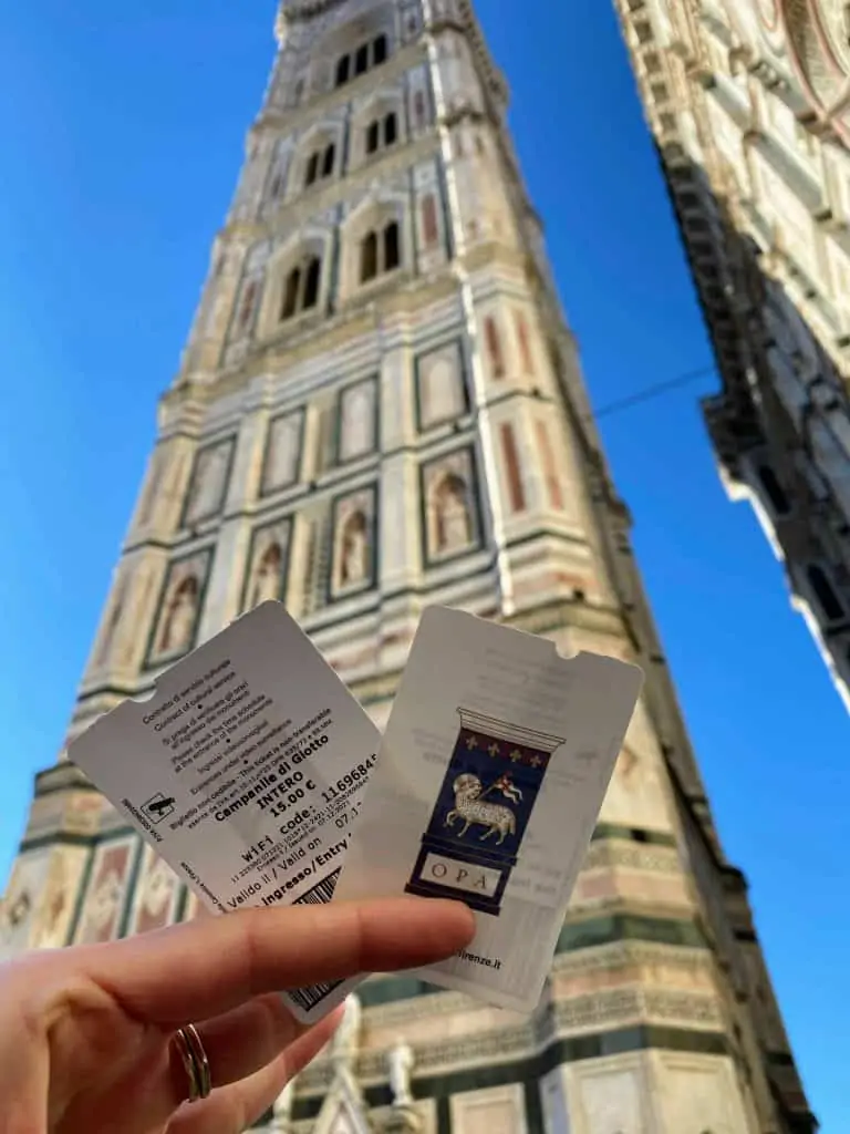 Close up of hand holding two ticket to climb Giotto's bell tower (Campanile di Giotto) in Florence, Italy.  In the background you can see the bell tower.