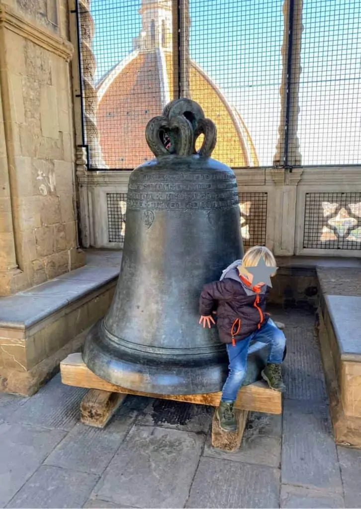 Child climbing next to bell on one of the viewing platforms in Giotto's bell tower in Florence, Italy.  In the background you can see the dome of Duomo.
