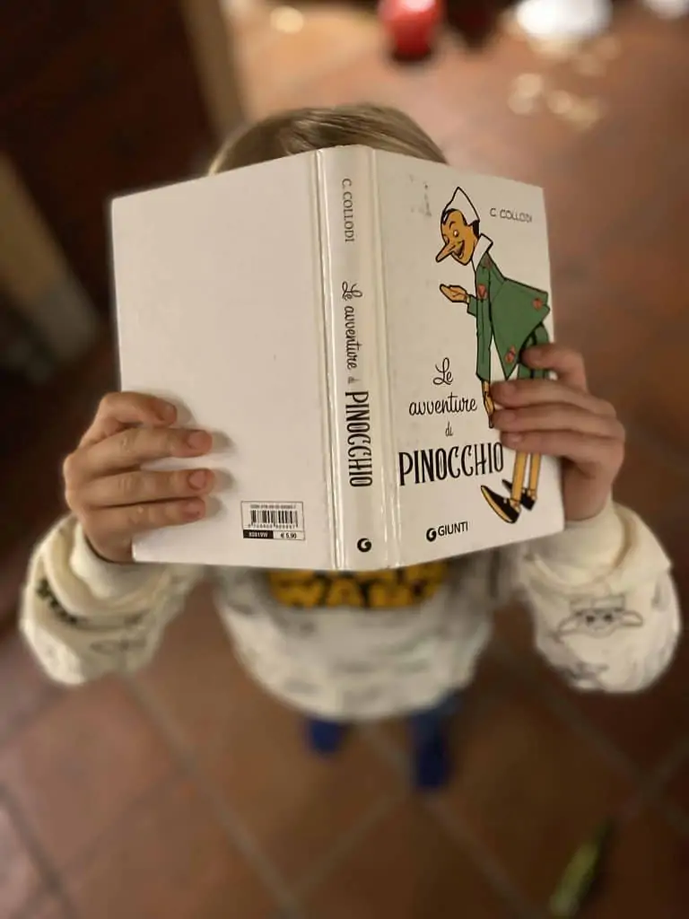 boy holding Avventure di Pinocchio book in front of his face.  The background is blurry.