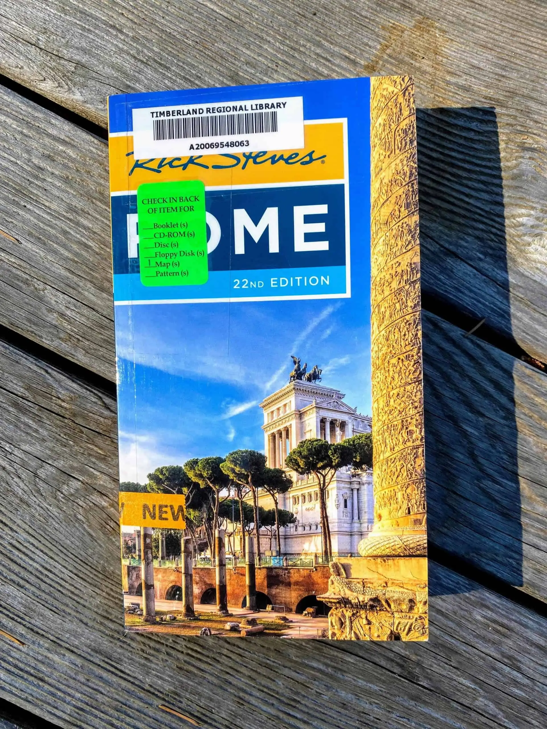 Library copy of Rick Steve's Rome guidebook with a wooden deck background.