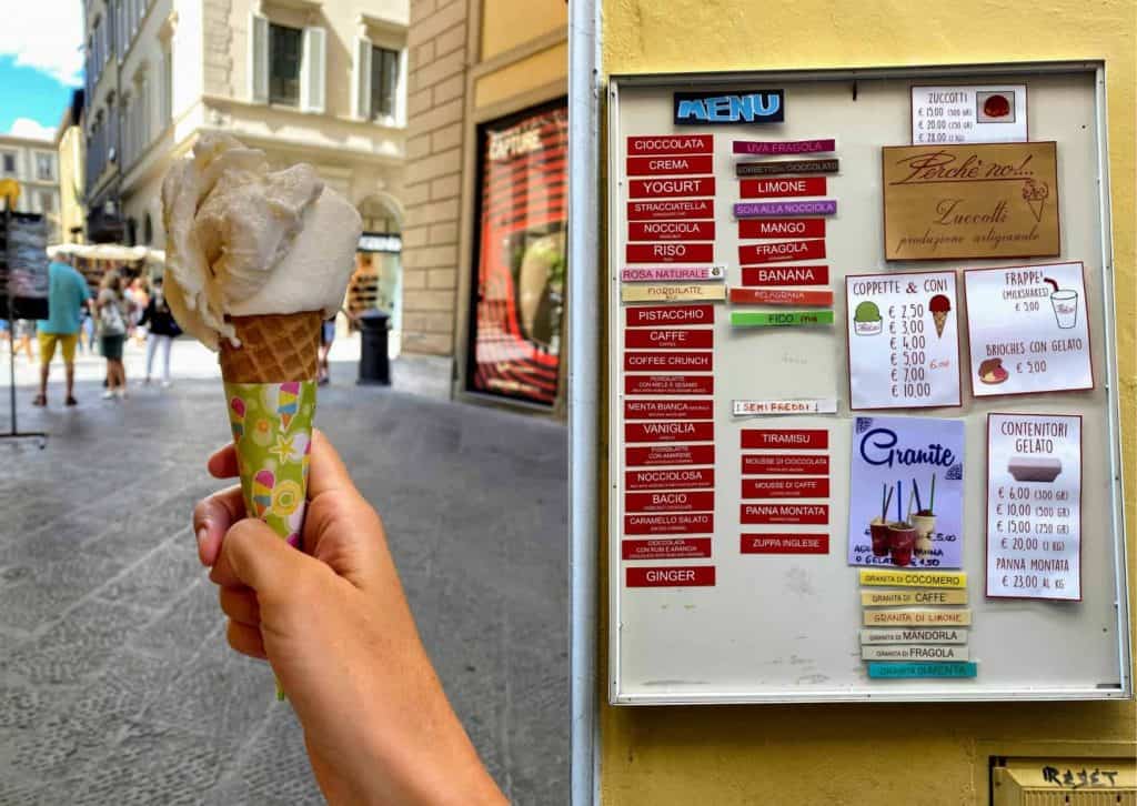 Hand holds up gelato cone in Florence. On right is sign with gelato flavors.