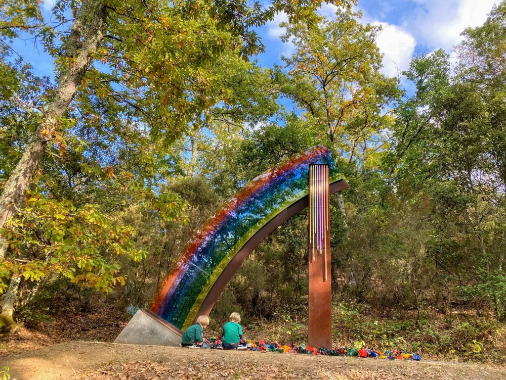Boys play with rainbow sculpture in forest.