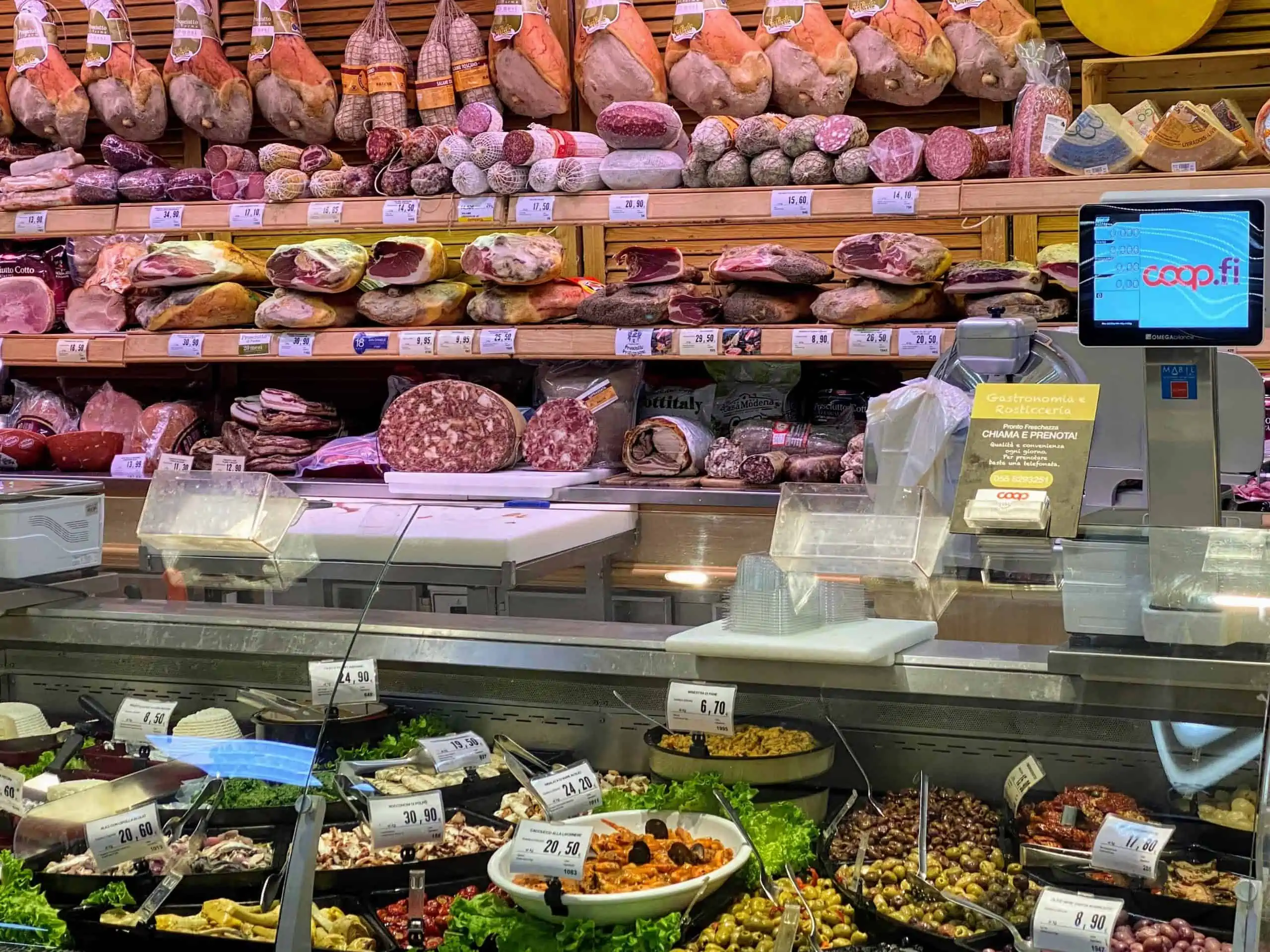 Deli section in an Italian grocery store. You can see cured meats on shelves and salads.