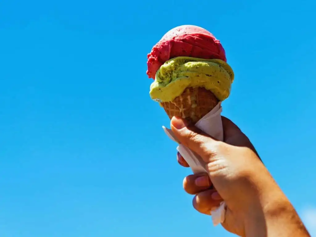 Hand holds cone of gelato against blue sky.