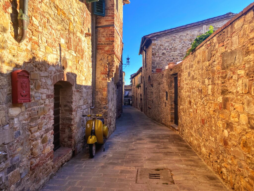 Vespa next to a wall on a small lane in San Donato in Poggio in Chianti, Italy.