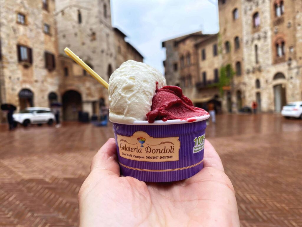 Hand holds a cup of gelato from Gelateria Dondoli in the main square of San Gimignano in Tuscany, Italy.
