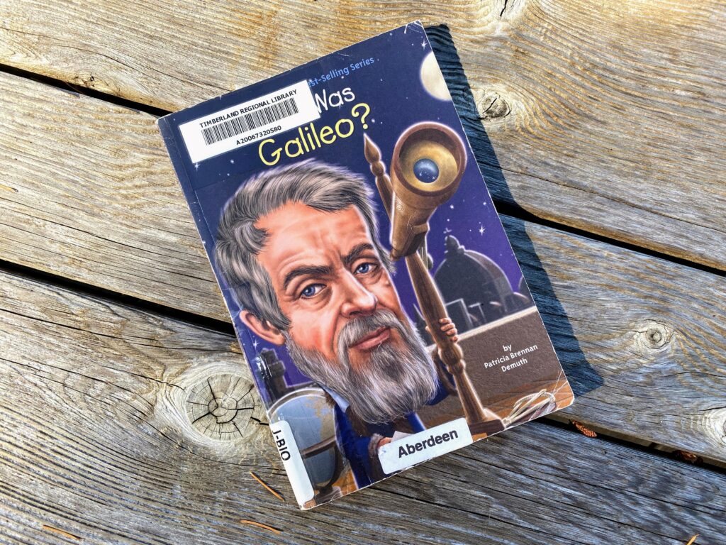 Who Was Galileo? kids' book on a wooden background.