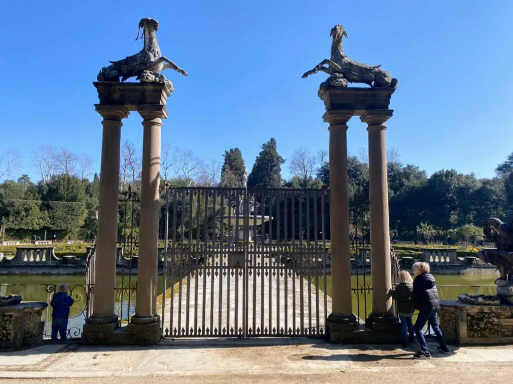 Boys looking out at the Fountain of the Ocean in Boboli Gardens.  There is a small gate with columns on either side, topped with statues.  