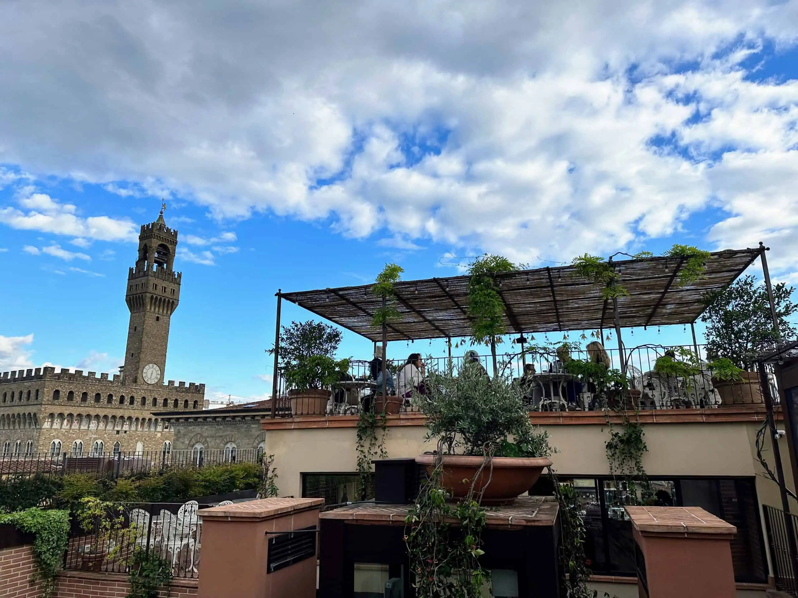 People sitting on a rooftop terrace at the Angel Rooftop Bar in Florence, Italy. You can see the Palazzo Vecchio on the left.