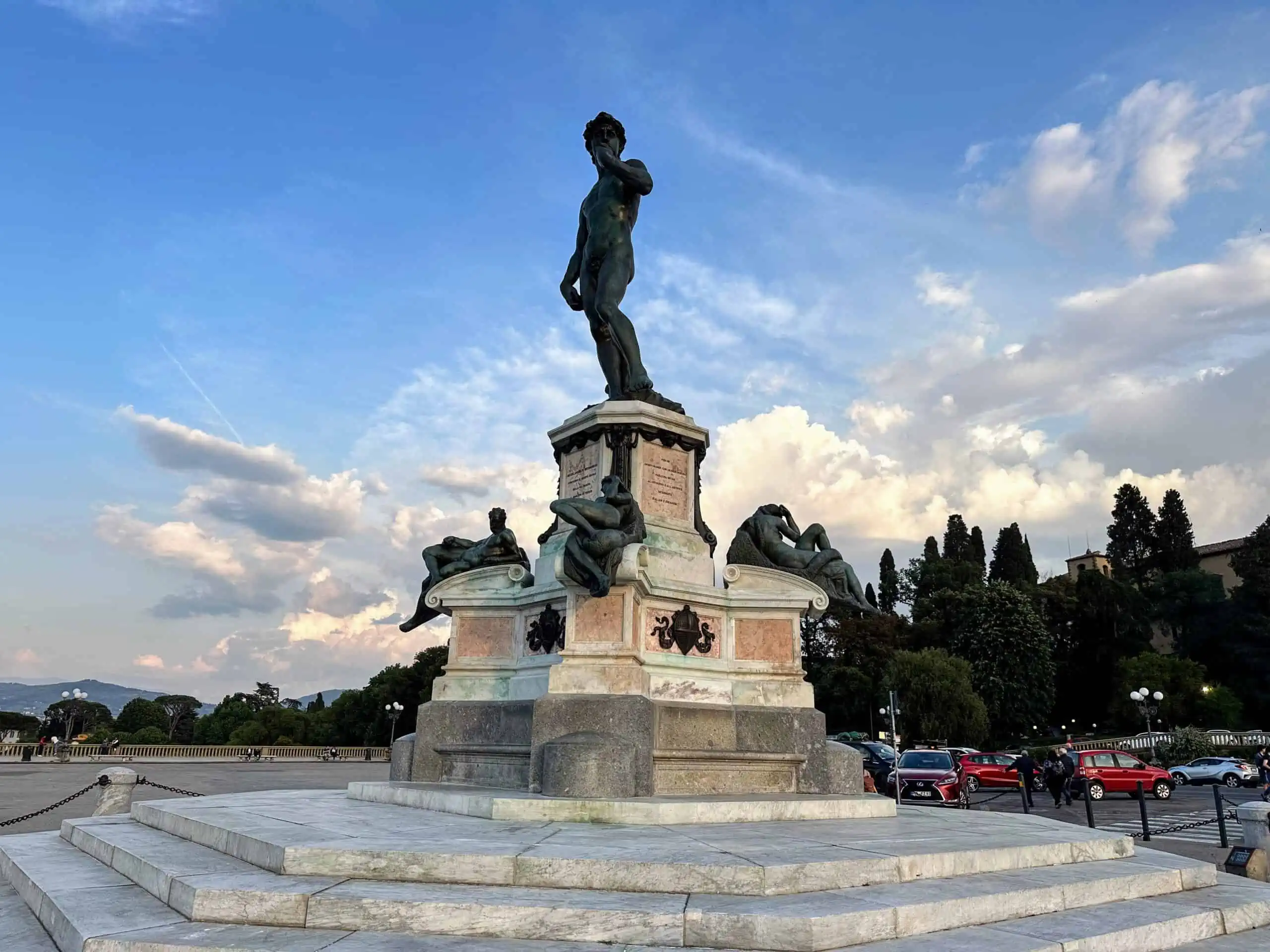 View of Michelangelo statue in Piazzale Michelangelo in Florence. It's a sunny day. You can see cars parked in the piazzale in the background on the right.