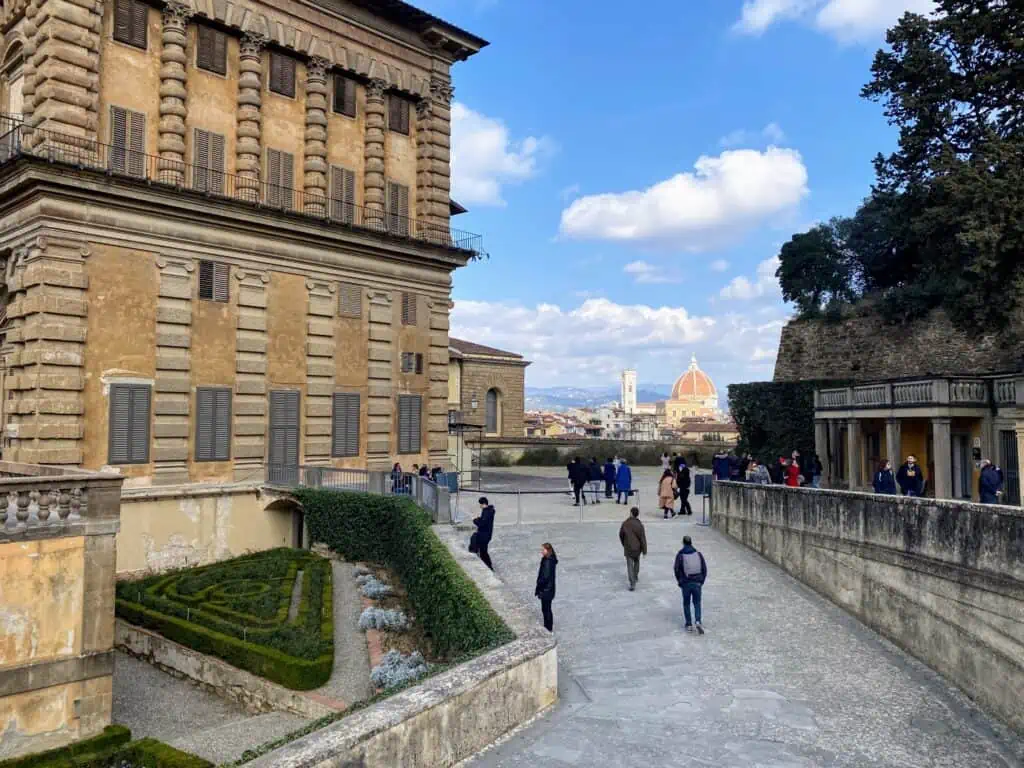 View of Florence Duomo and bell tower peeking between building and wall in the Boboli Gardens.