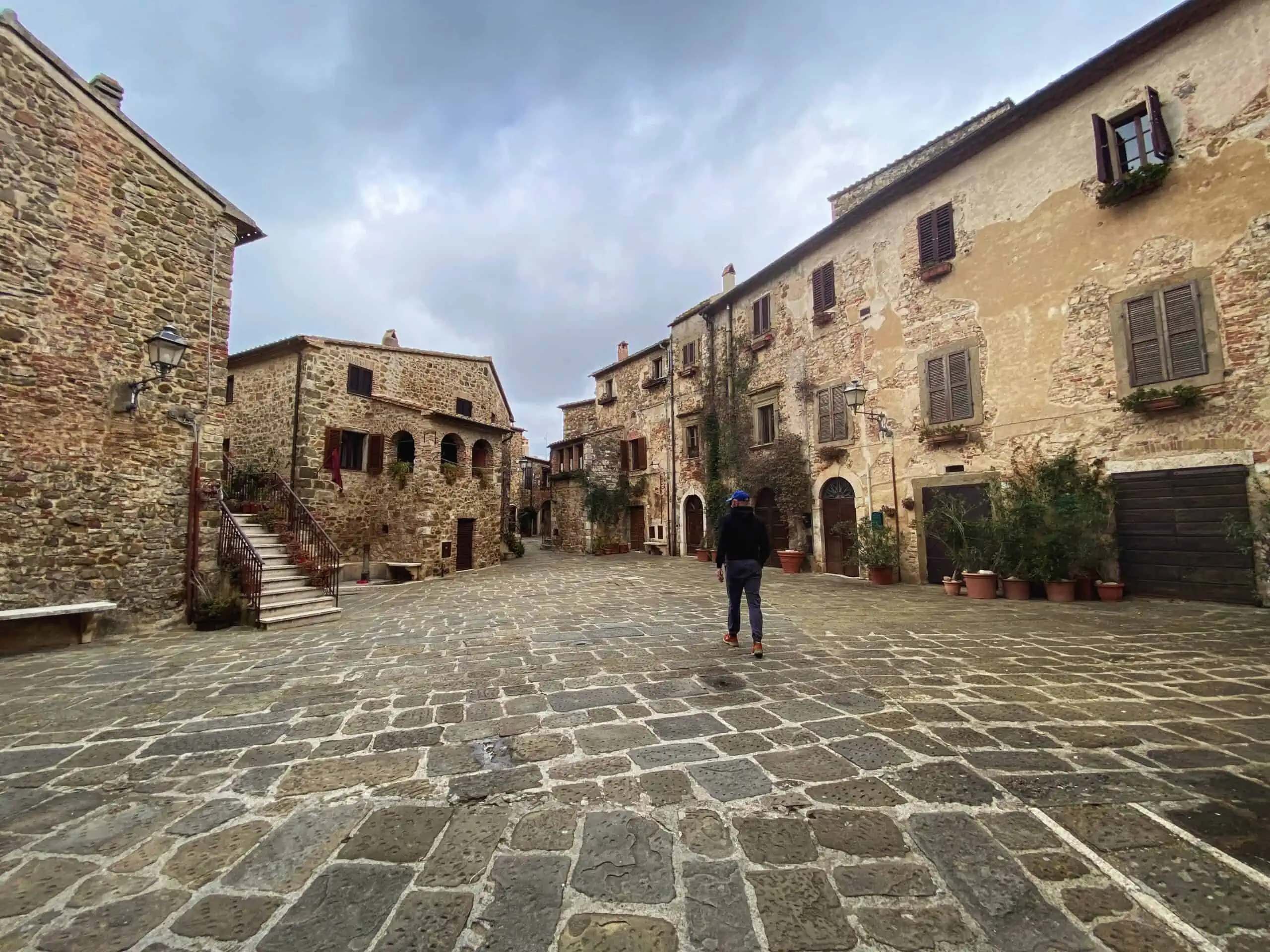 Man walking in Piazza del Castello in Montemerano, Tuscany. It's a cloudy day.