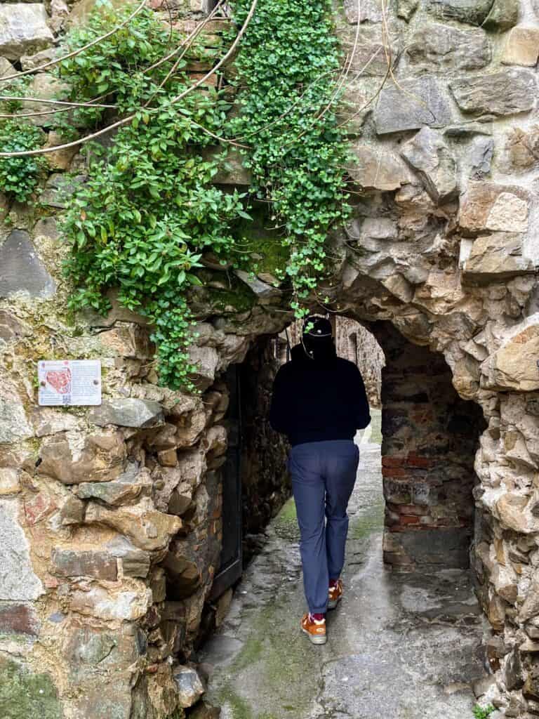 Man ducks to walk through Porta La Buca in Montemerano, Tuscany, a stone entrance into the village.