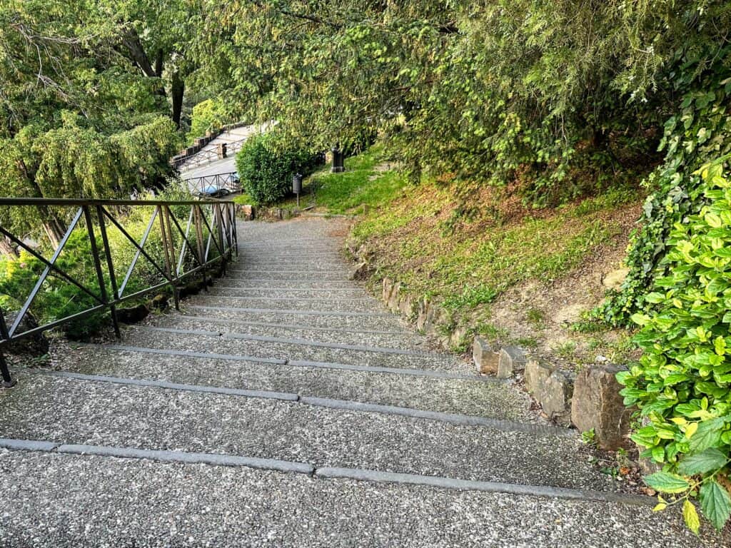 Stone steps on the path between Florence city center and Piazzale Michelangelo. There are trees and bushes on both sides.
