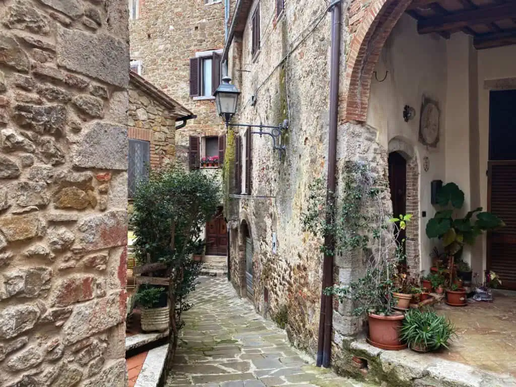 Narrow lane in medieval village of Montemerano in Tuscany. You can see the history in the many layers of stones and bricks in the walls. There are plants and flowers on the street and in the windows.