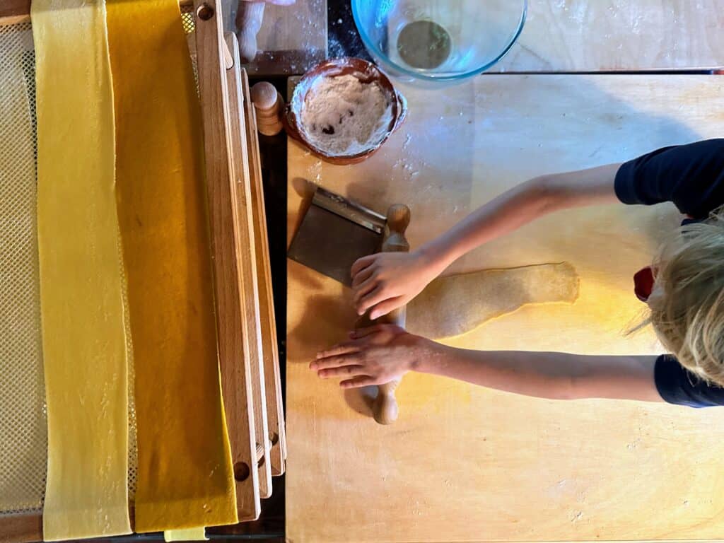 View from above of boy rolling out fresh pasta. On right you can see freshly rolled pasta drying on racks.