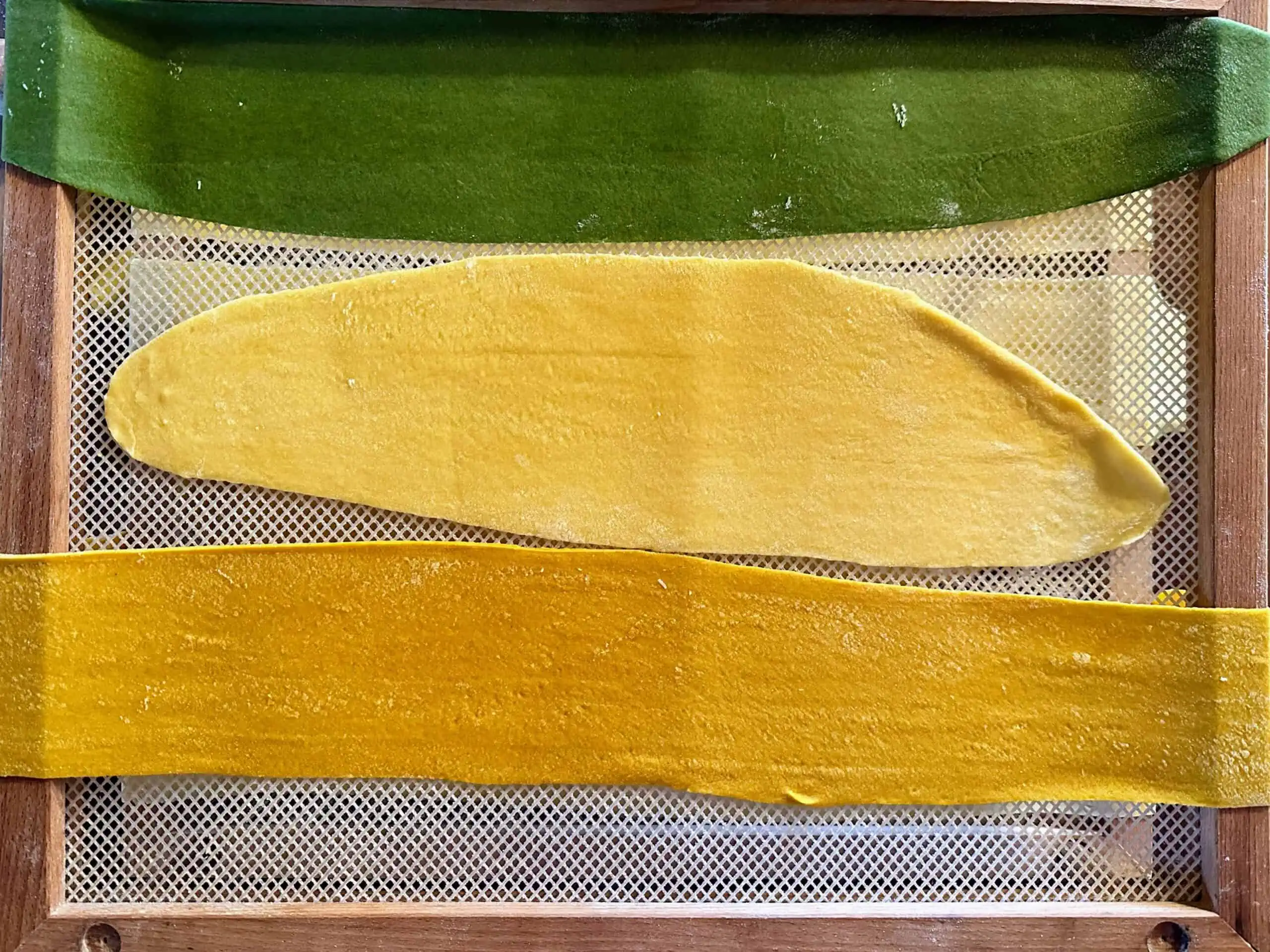 Fresh pasta tinted green and yellow (plus some not tinted) drying on a rack.