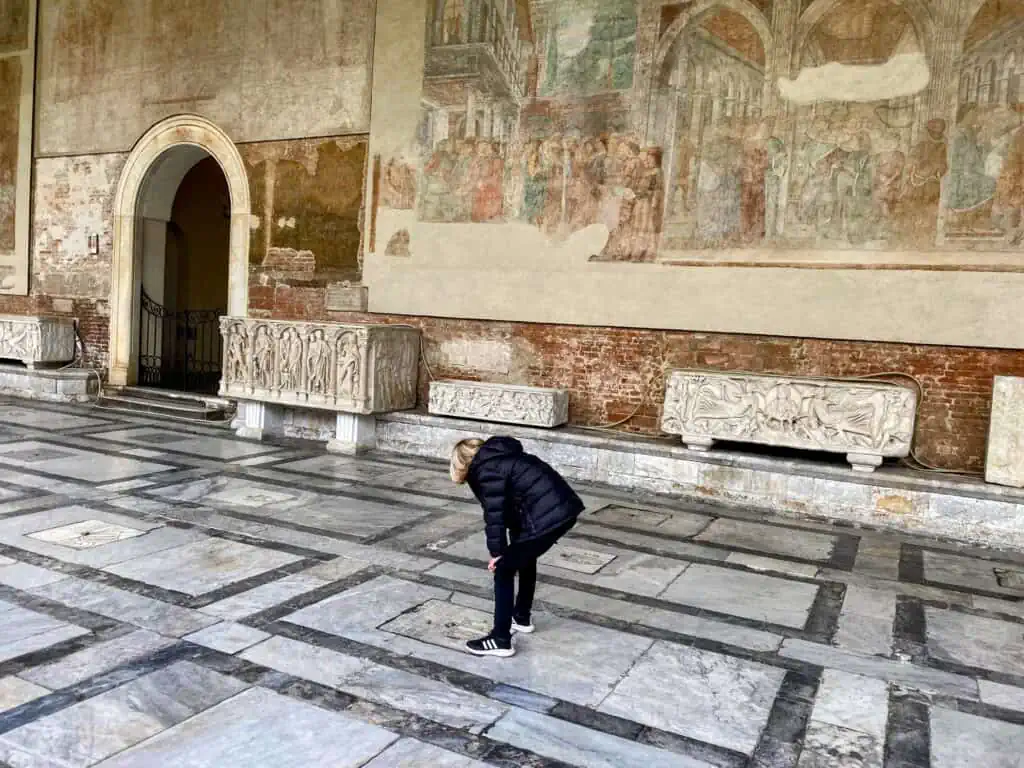 Boy exploring the tombs at the Camposanto in Pisa, Italy. You can see frescoes on the wall in the background.
