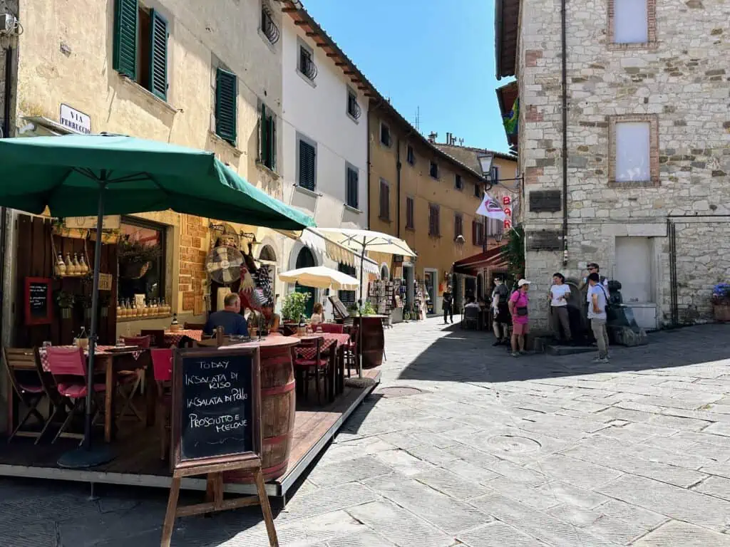 Pedestrian center of Castellina in Chianti in Tuscany, Italy. You can see stone buildings and in the foreground a restaurant with an outdoor eating area.