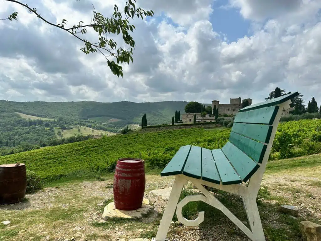 Large green bench overlooking a vineyard in Tuscany. Castello di Meleto in background.