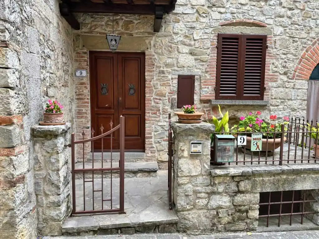 Entrance to home in Italy. Stone building with small gate at entrance, close to wooden door. Plants decorate the entrance.