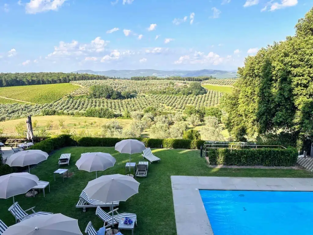 Corner of pool, grassy area with umbrellas and loungers, and vineyard views at Castello del Nero in Chianti, Tuscany, Italy.