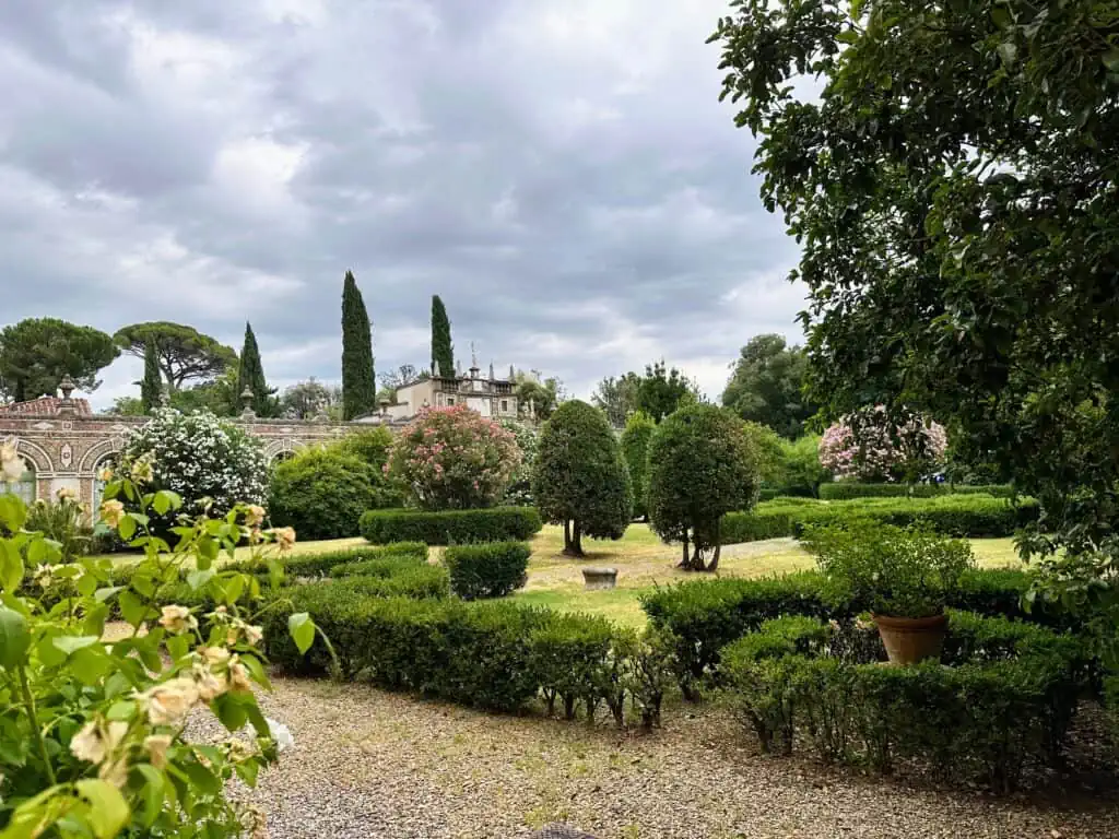 Gardens at Four Seasons Hotel in Florence, Italy. You can see bushes, and some flowers. There is a gravel path in the foreground.