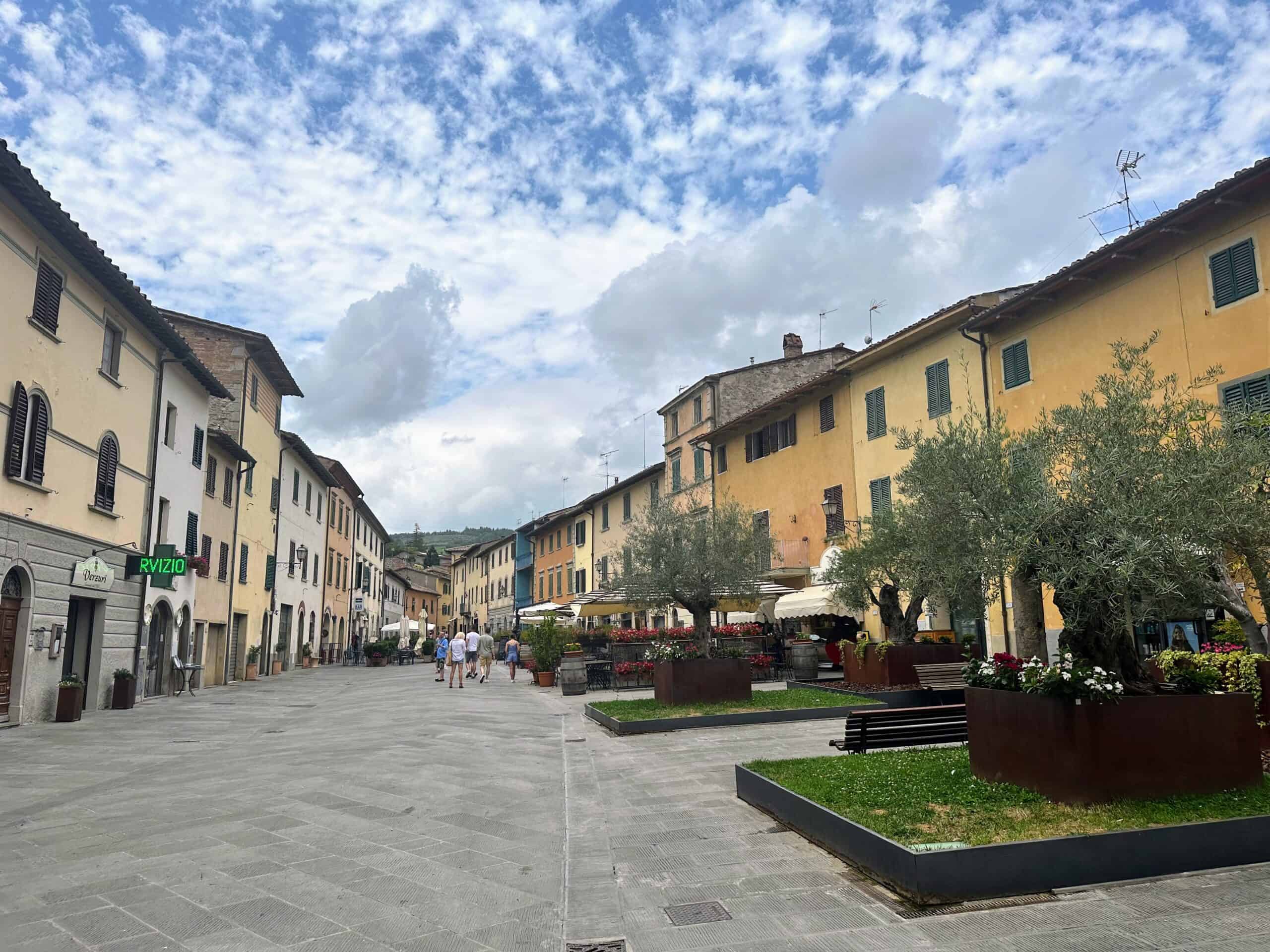 Main piazza in Gaiole in Chianti on a sunny day. There are a few people walking at the end of the square.