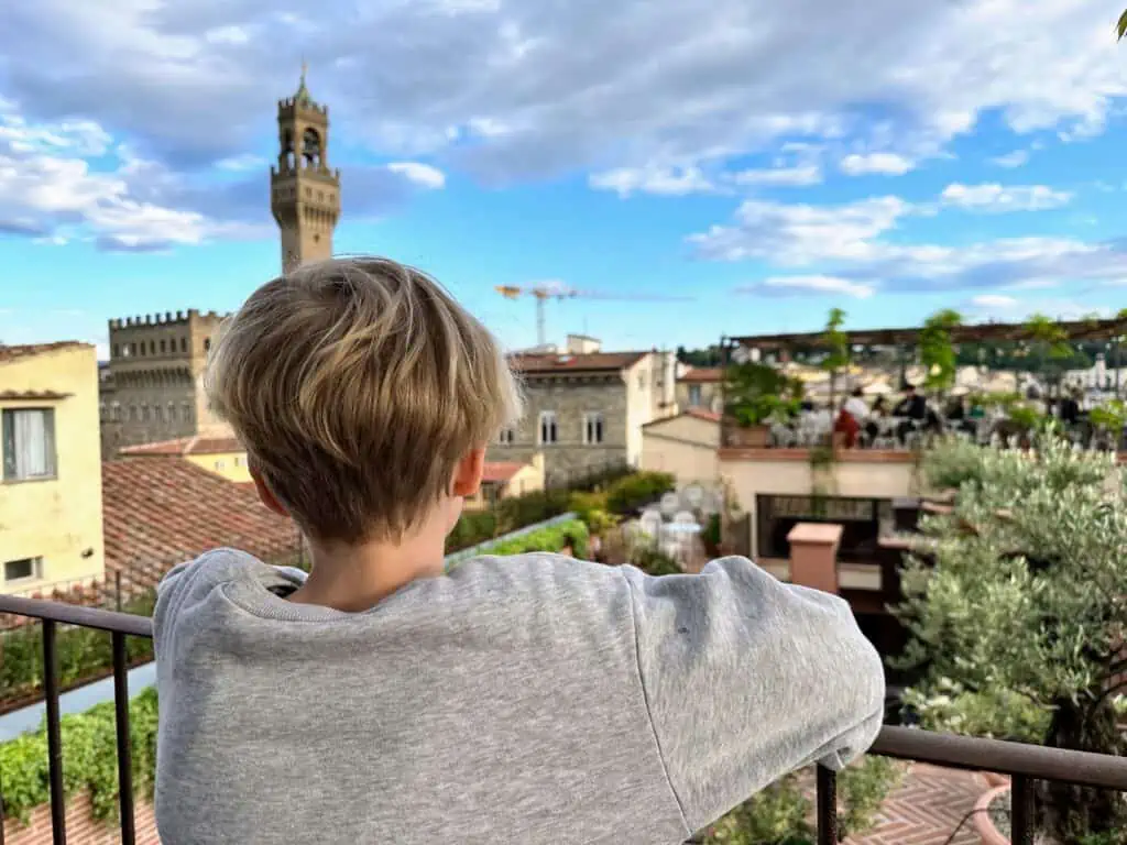 Boy looks out over rooftop railing at Florence, Italy skyline.