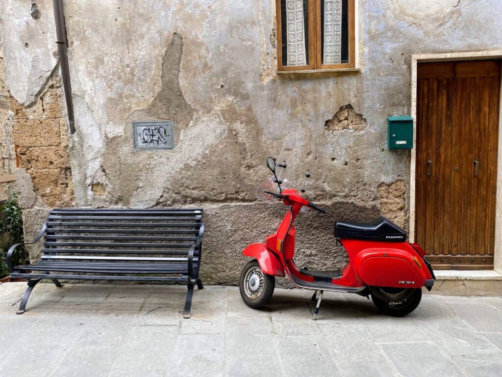 Red vespa sitting against a wall in Tuscany.