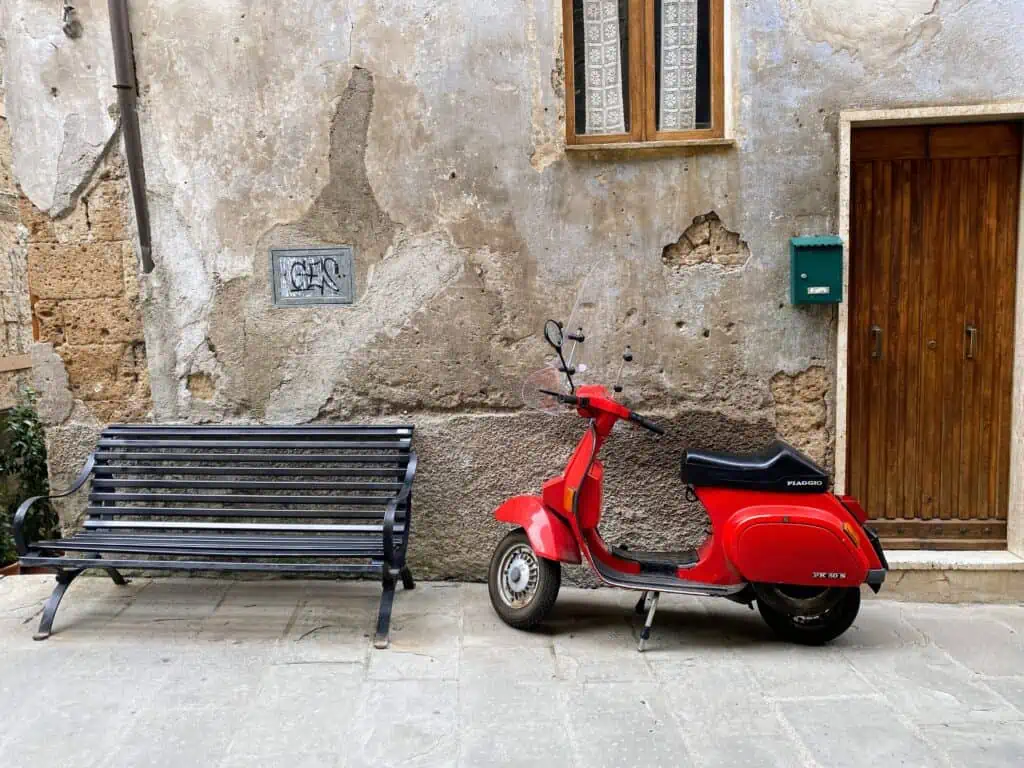 Red vespa sitting against a wall in Tuscany.