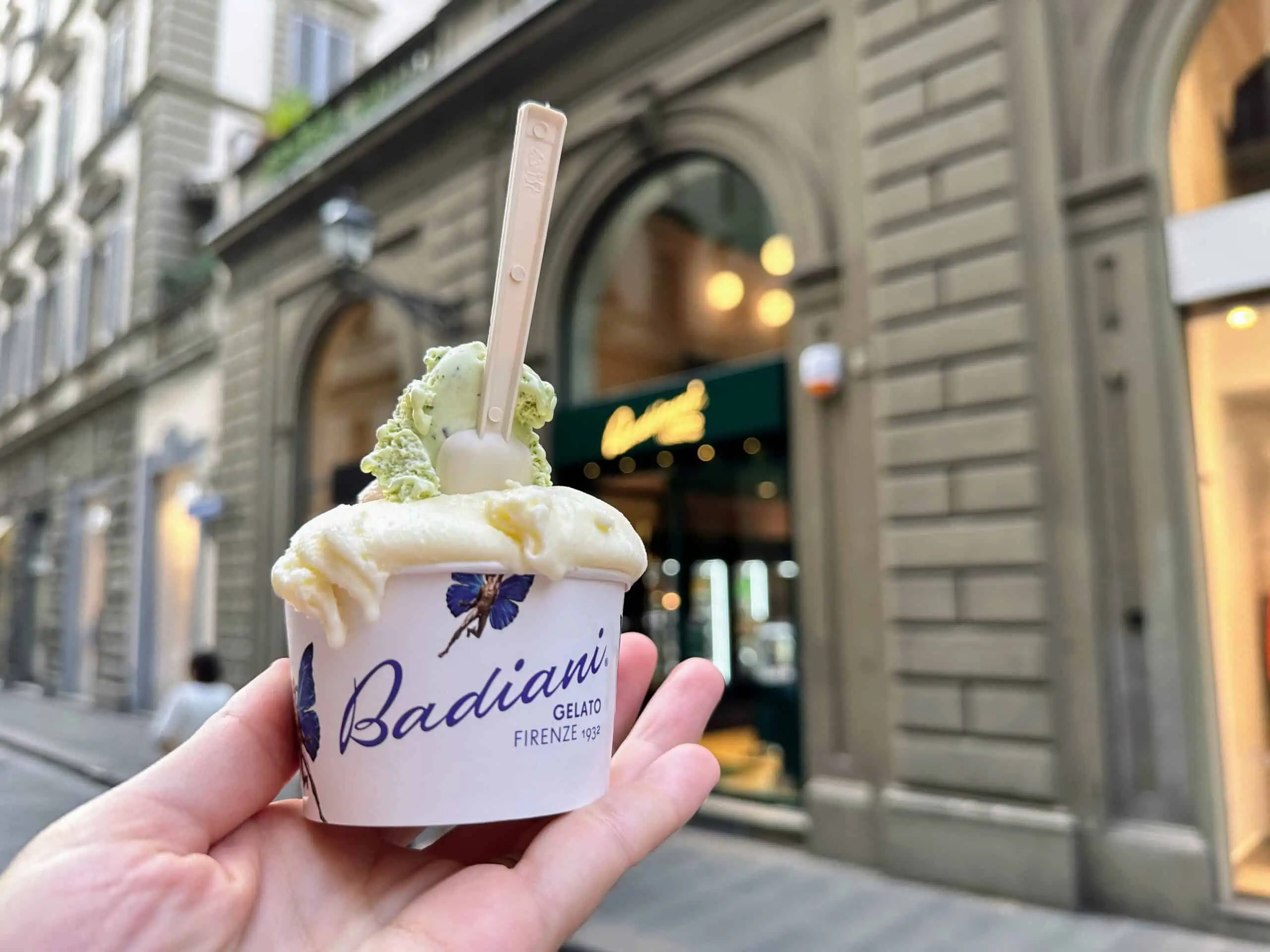 Hand holding cup of Badiani gelato in front of the shop in Florence, Italy.