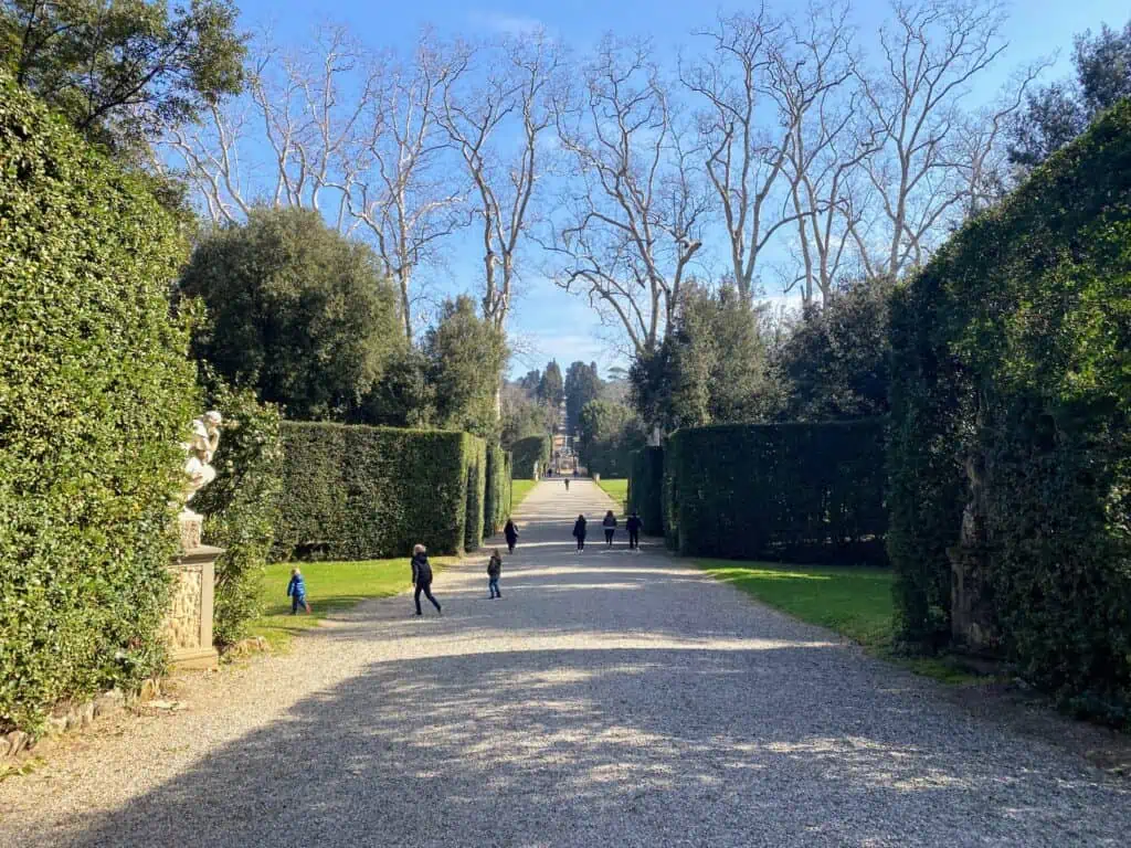 Boys running on a path in Boboli Gardens. Gravel path with tall bushes on either side.