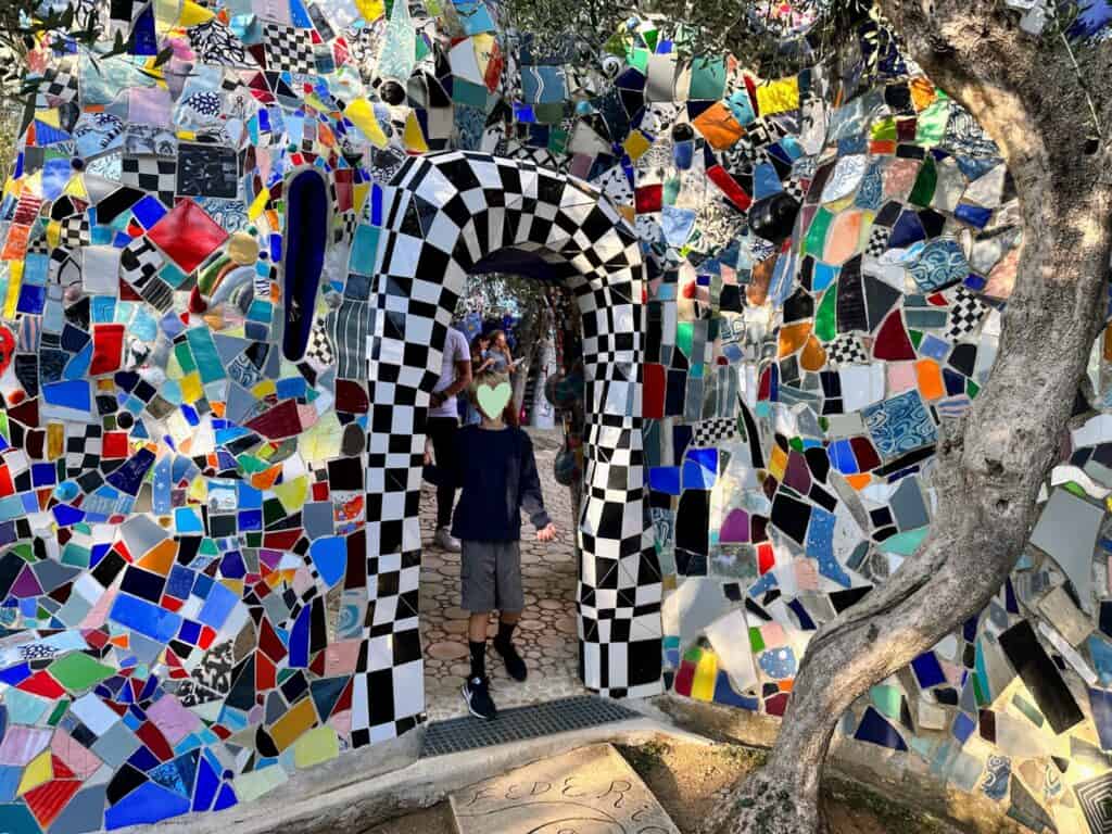 Colorful tiles and mosaics form walls and an archway. Boy stands in arch.