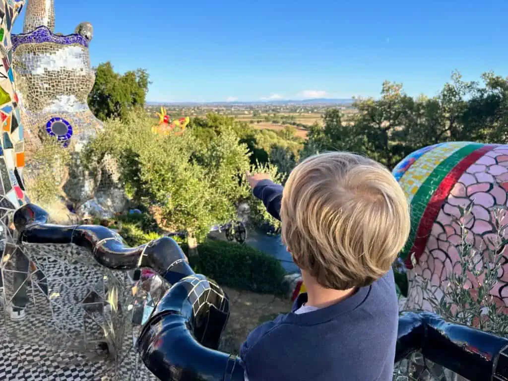 Boy pointing to colorful sculptures at the Tarot Garden in Tuscany, Italy.