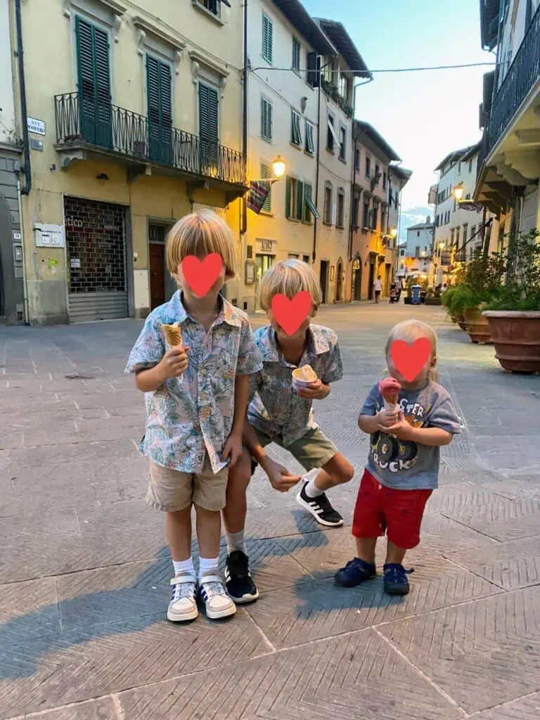 Three boys eating gelato in a small Italian village. You can see buildings on either side. Graphic hearts over boys' faces.