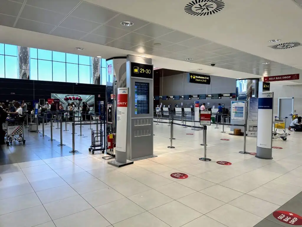 View of the check-in desks at the Florence, Italy airport. There are people waiting in a line on the left. It's a small area.