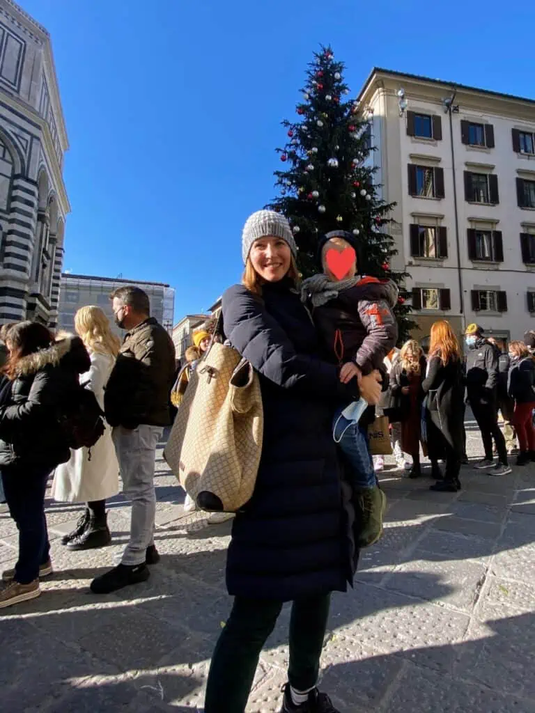 Mother holding son in front of Christmas tree in Florence, Italy's Piazza Duomo. People waiting in a line behind them.