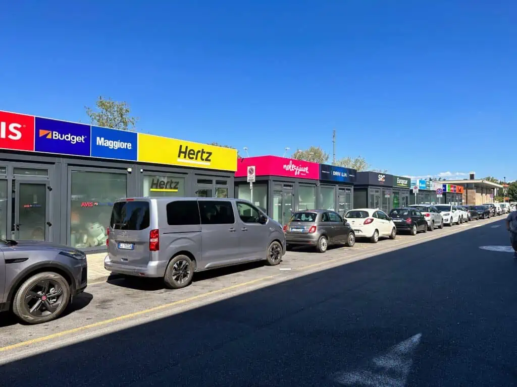Colorful signs for car rental companies at the employee booths in the parking lot of the Florence airport car rental location.